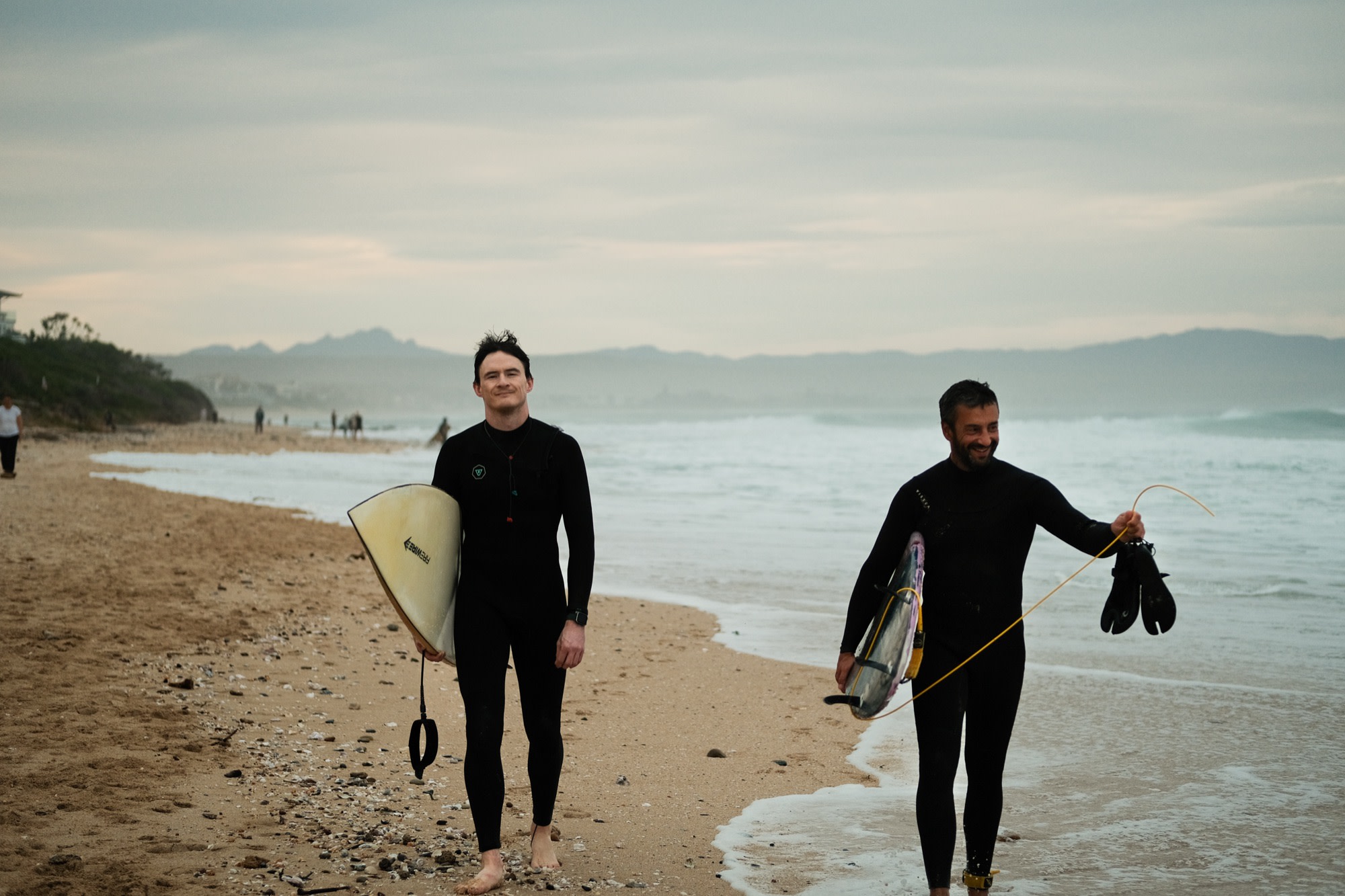 Two friends walking the beach with their boards
