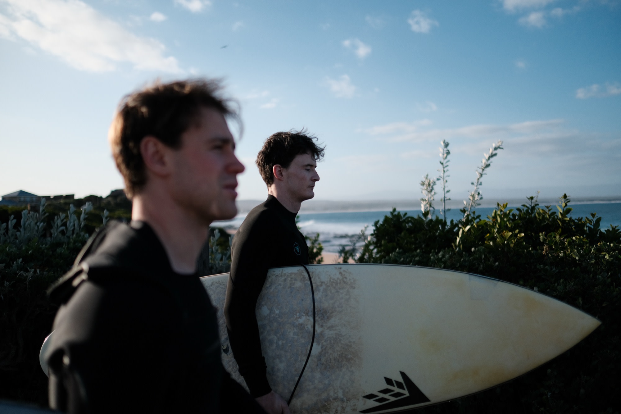 Two friends heading out to surf at dusk