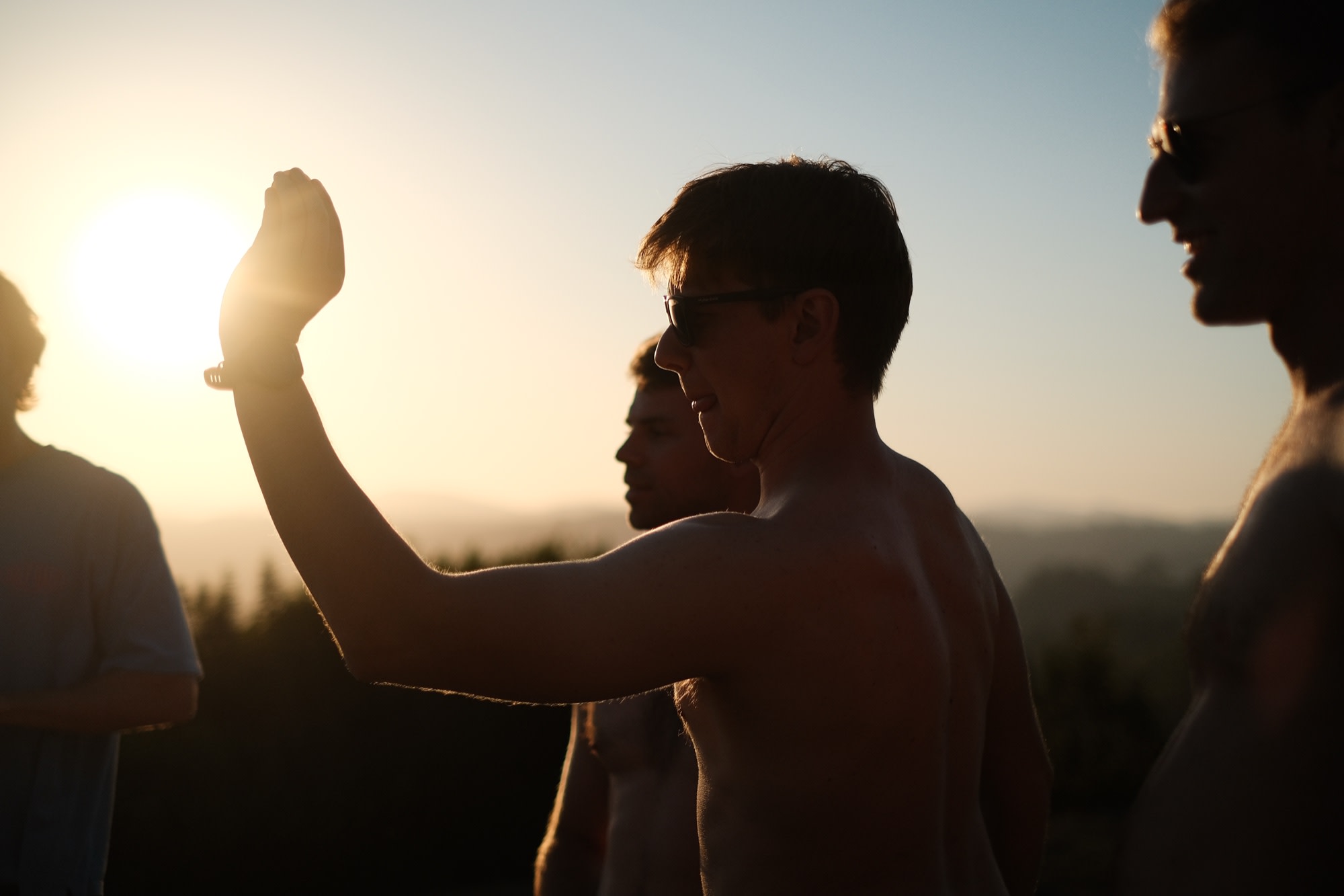 A friend eclipsing the setting sun with his fist, mates gathered around