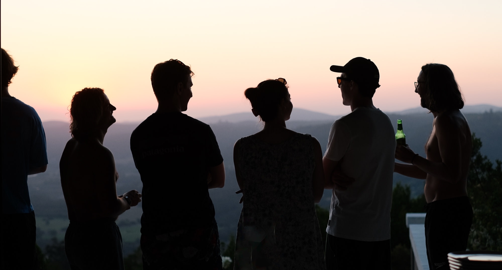 Friends silhouetted with a cold beer against a pink sunset