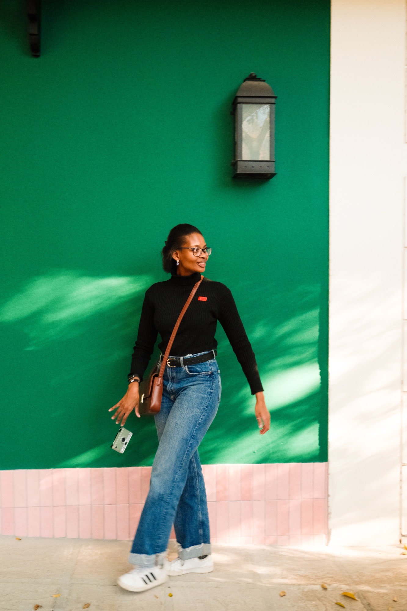 Kea walking past a green wall, film camera in hand
