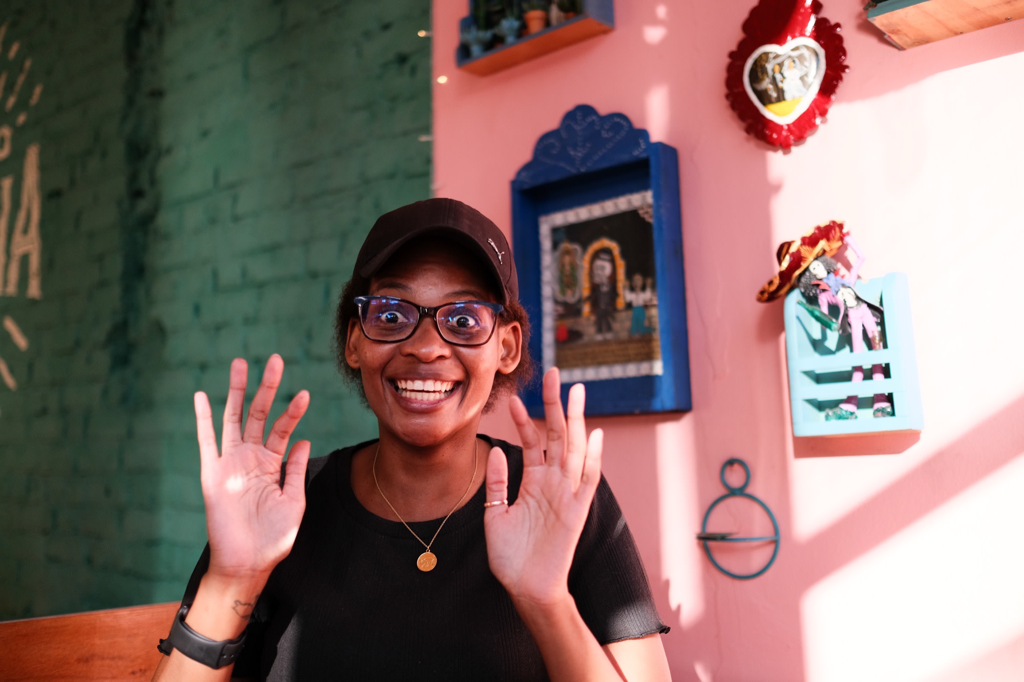 Kea laughing, hands raised, in a colourful café