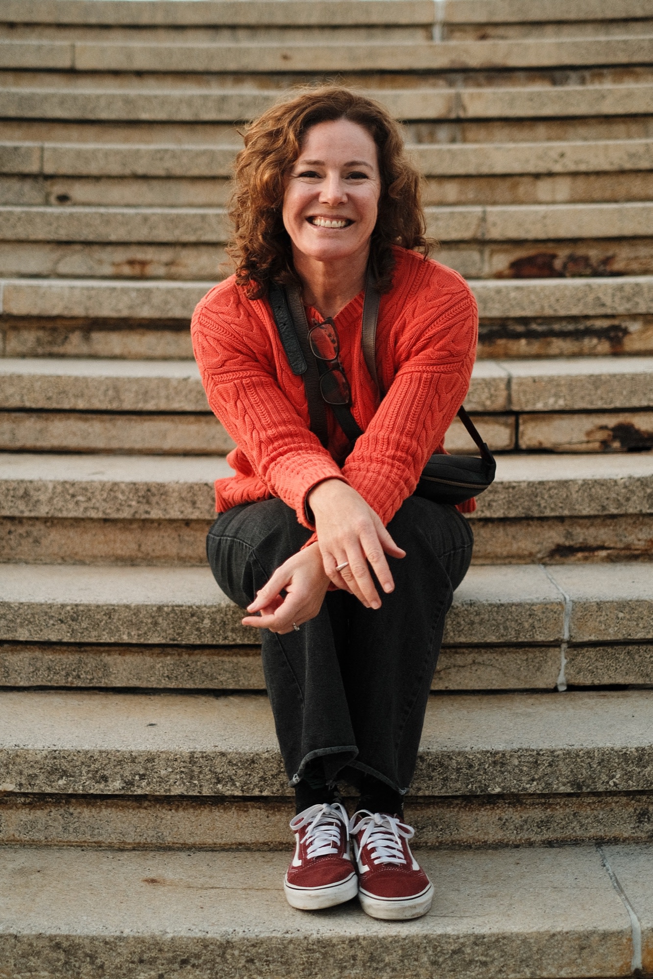 A warm smile on the stone steps in a coral jumper