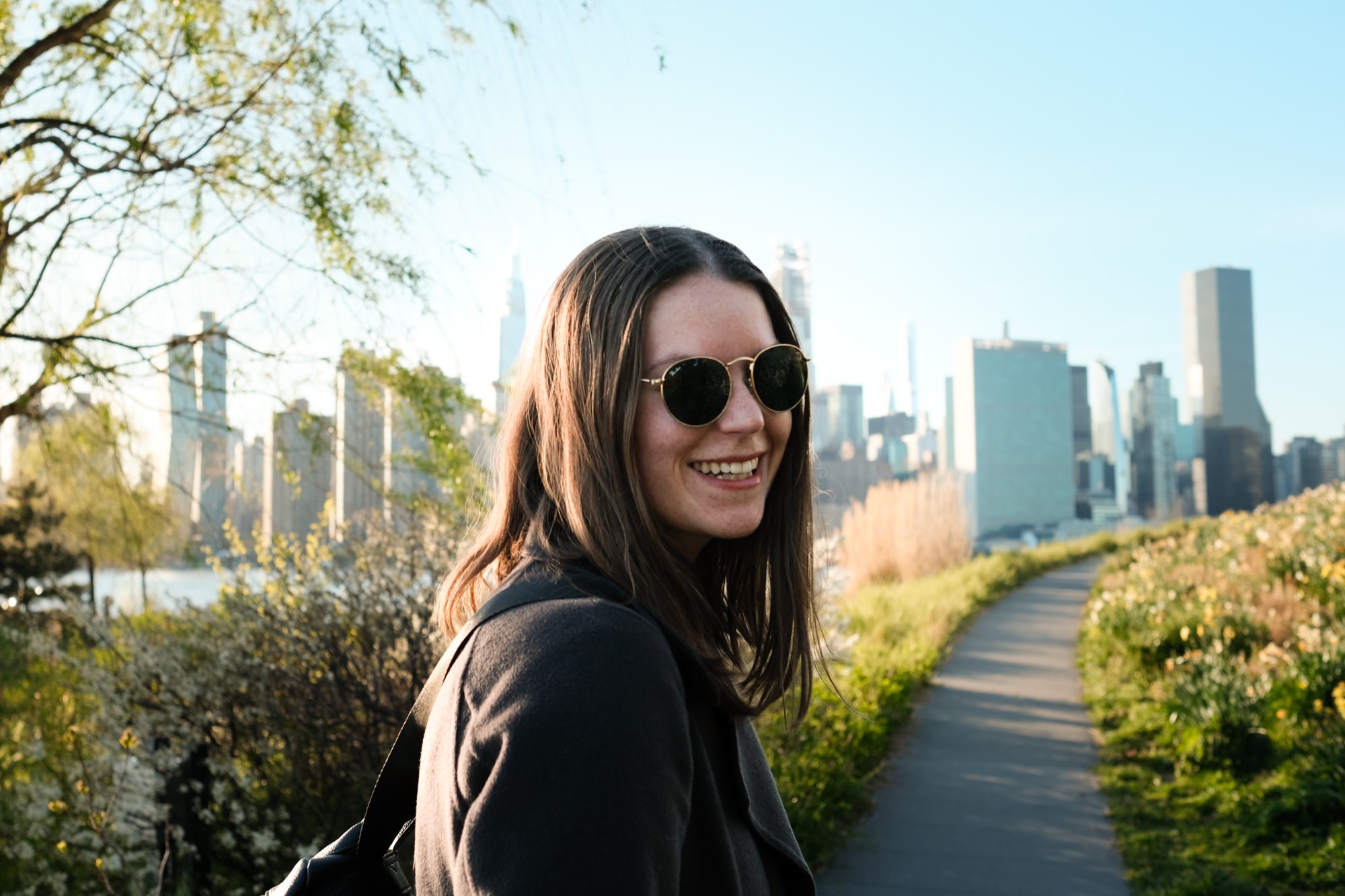 A sunlit smile on a riverside path, city skyline behind