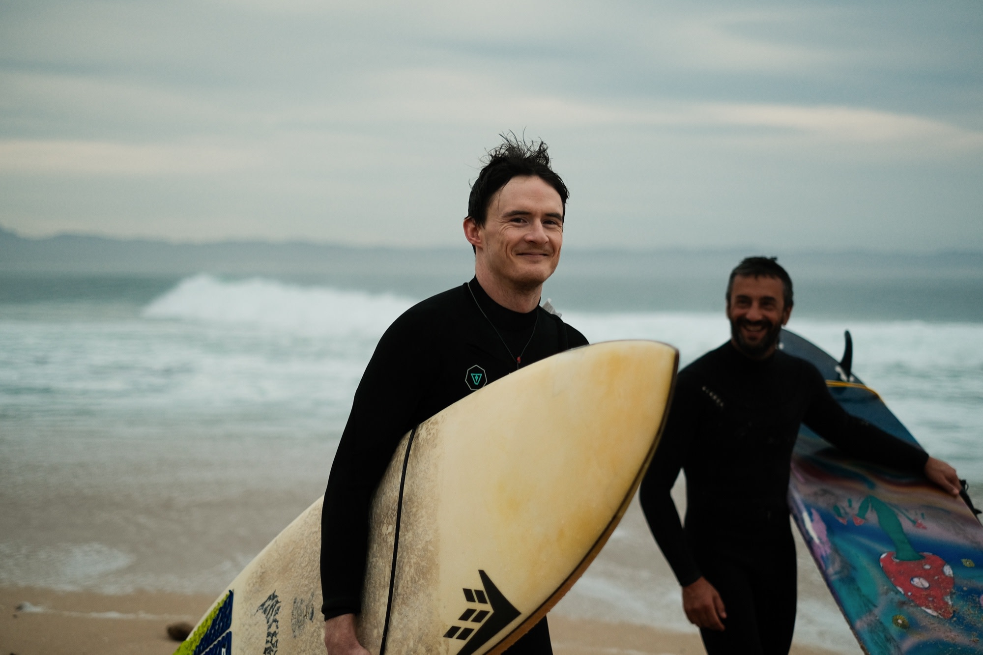 In from a surf, board underarm, a mate close behind