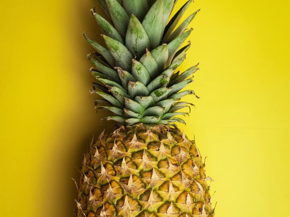 Whole ripe pineapple against a bright yellow background.