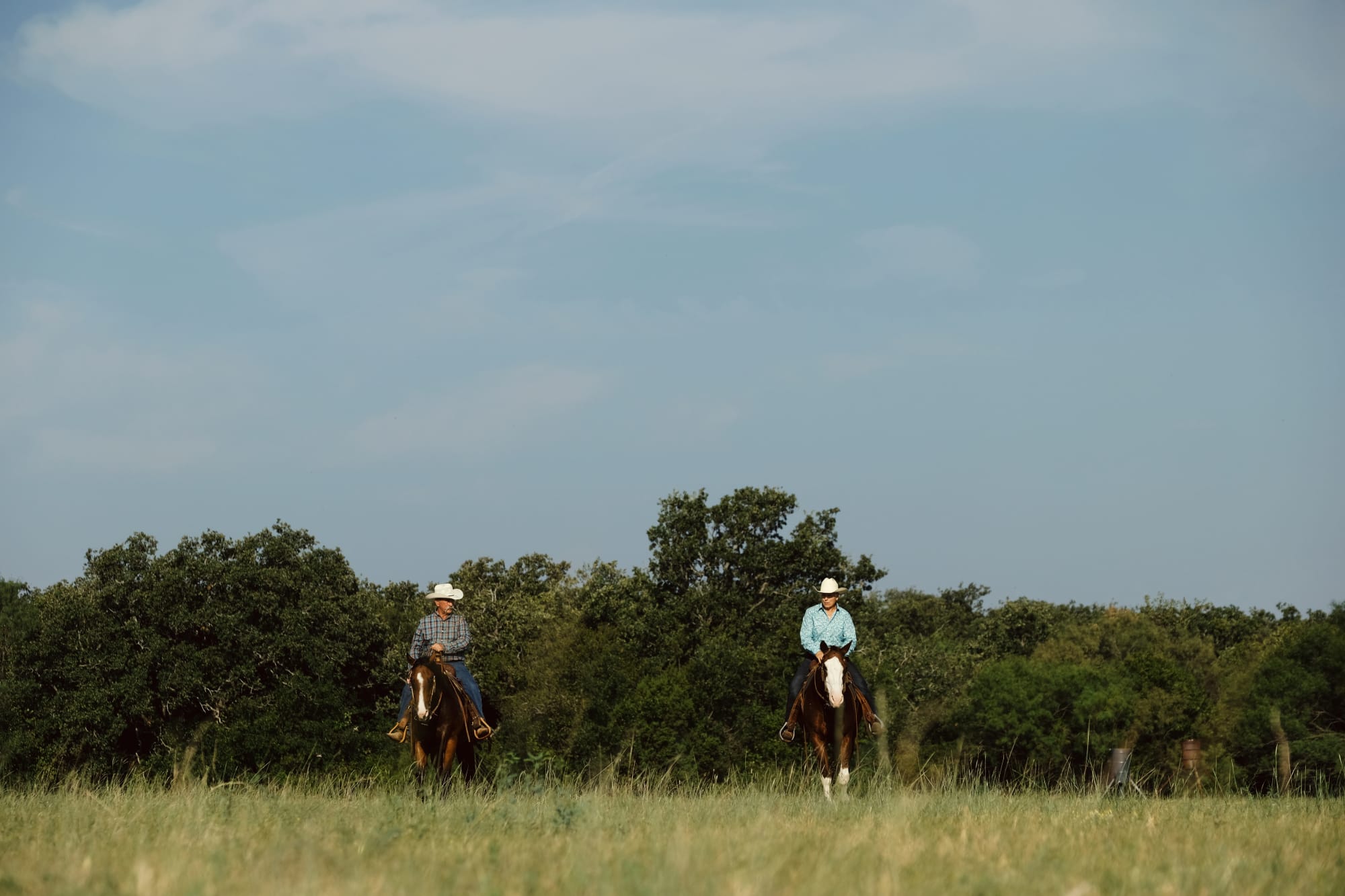 Two riders on horseback crossing a grassy meadow beneath a wide sky