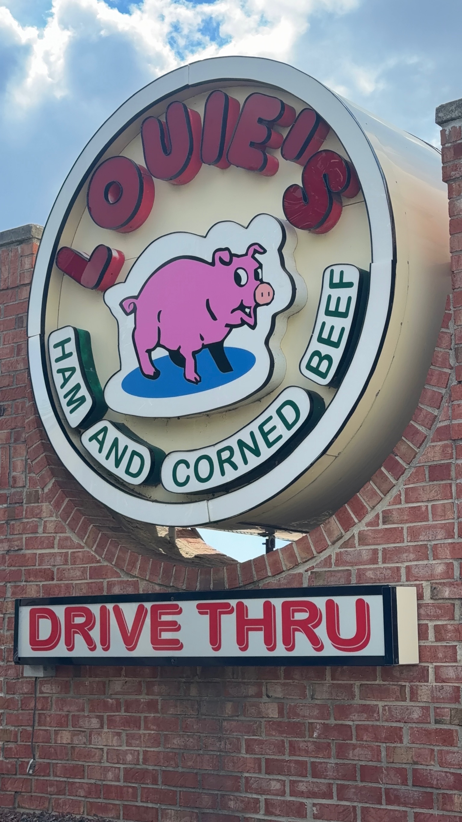Louie's Ham and Corned Beef sign above the Drive Thru sign on the brick building