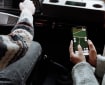Dua orang di dalam kendaraan saat perjalanan darat; seorang penumpang memegang ponsel untuk membaca aplikasi peta dan navigasi, sementara pengemudi tetap mengarahkan kendaraan.