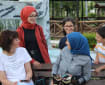Seorang perempuan lansia, dua perempuan dewasa, dan dua anak berkumpul serta mengobrol di bangku taman dengan air mancur dan rumput hijau di latar.