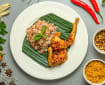 Hidangan ayam betutu berbumbu merah dengan nasi di atas piring beralas daun pisang, dikelilingi bahan bumbu seperti cabai, serai, bawang, dan kunyit.