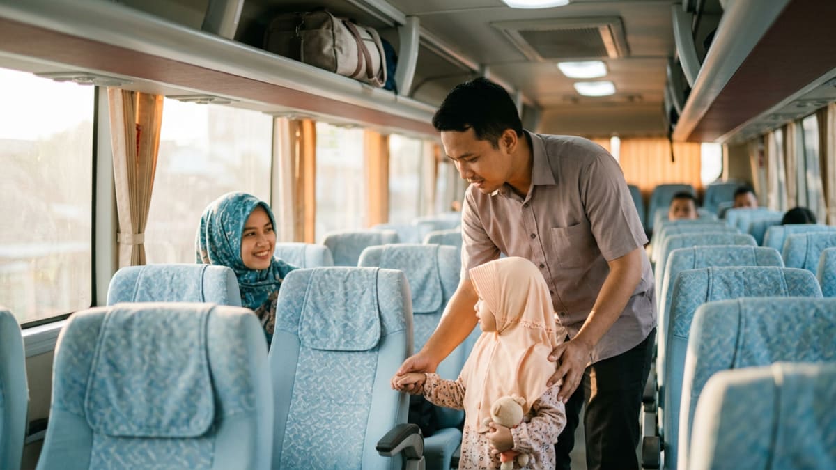 Ilustrasi keluarga Indonesia di dalam interior bus AKAP: seorang ayah menggandeng putrinya yang berhijab menuju kursi, sementara sang ibu tersenyum dari kursi dekat jendela.
