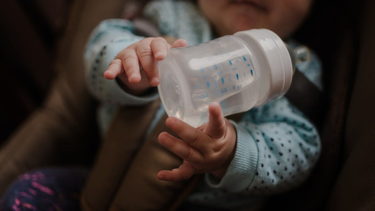 Anak kecil memegang botol di kursi pengaman mobil