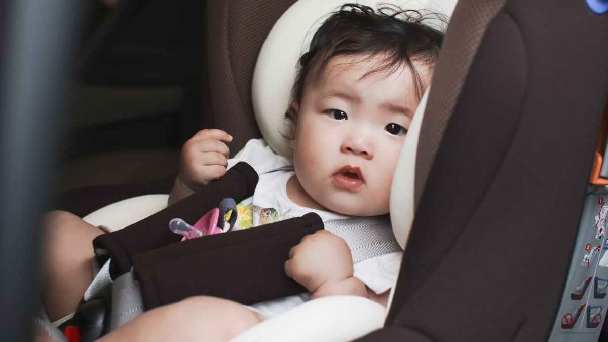 Bayi duduk tenang di car seat dengan tali pengaman lima titik terpasang.