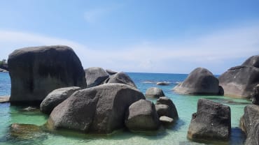 Batu granit raksasa menjorok ke perairan jernih biru kehijauan di Pantai Tanjung Tinggi, Belitung, pada hari yang cerah.