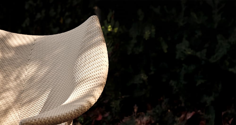 Wicker chair in front of a dark leafy background