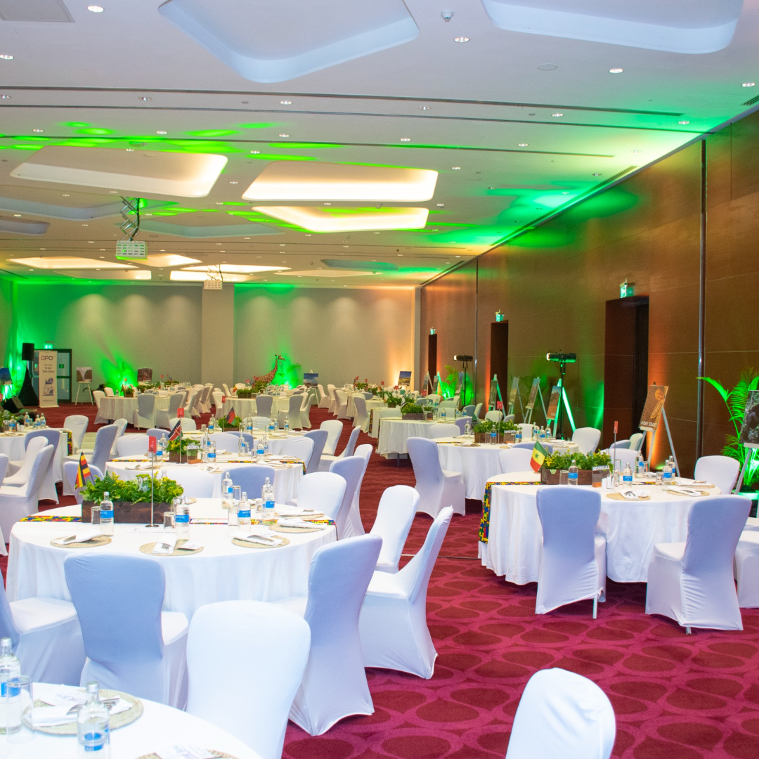 Fairy-lit stretch tent over white-clothed round tables with green organza centrepieces