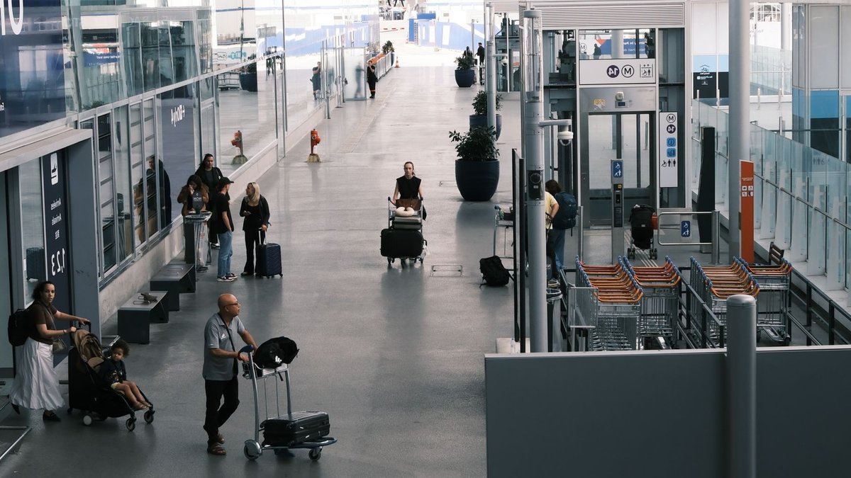 Travelers navigate an airport terminal corridor with luggage carts and suitcases.