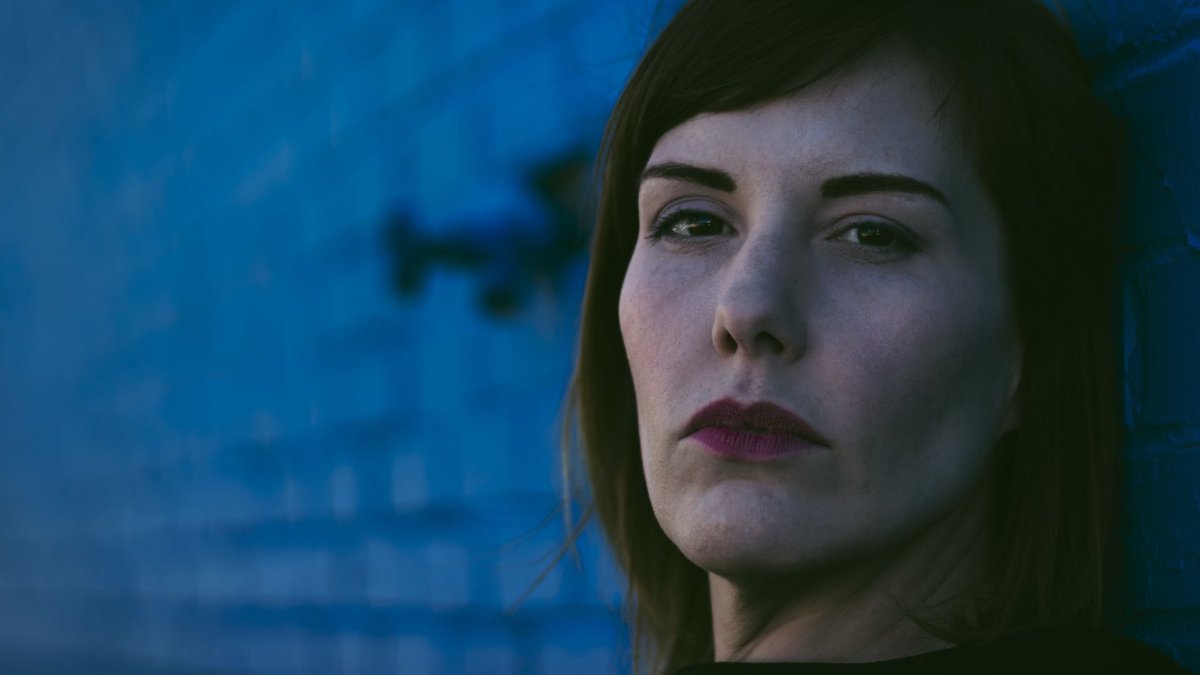 Jeweler Couple Donates 38-Acre Park to Fayetteville A woman with brown hair poses at night against a blue brick wall in Fayetteville, AR.