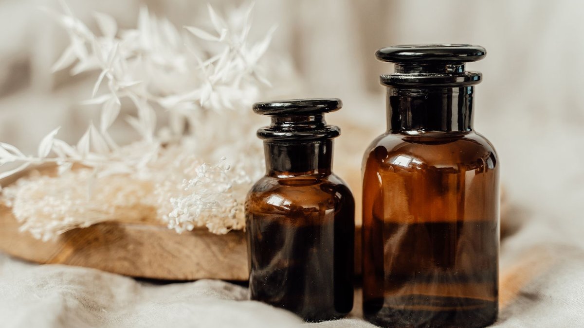 Molton Brown Opens First UK Scent Pavilion in Kent Brown glass aromatherapy bottles with white flowers in a calming still life composition.