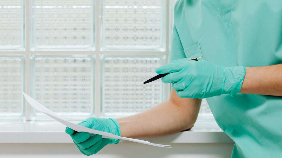 AI platform unifies hospital data to cut errors and costs A healthcare worker in scrubs and gloves holding a pen and paper in a medical facility.
