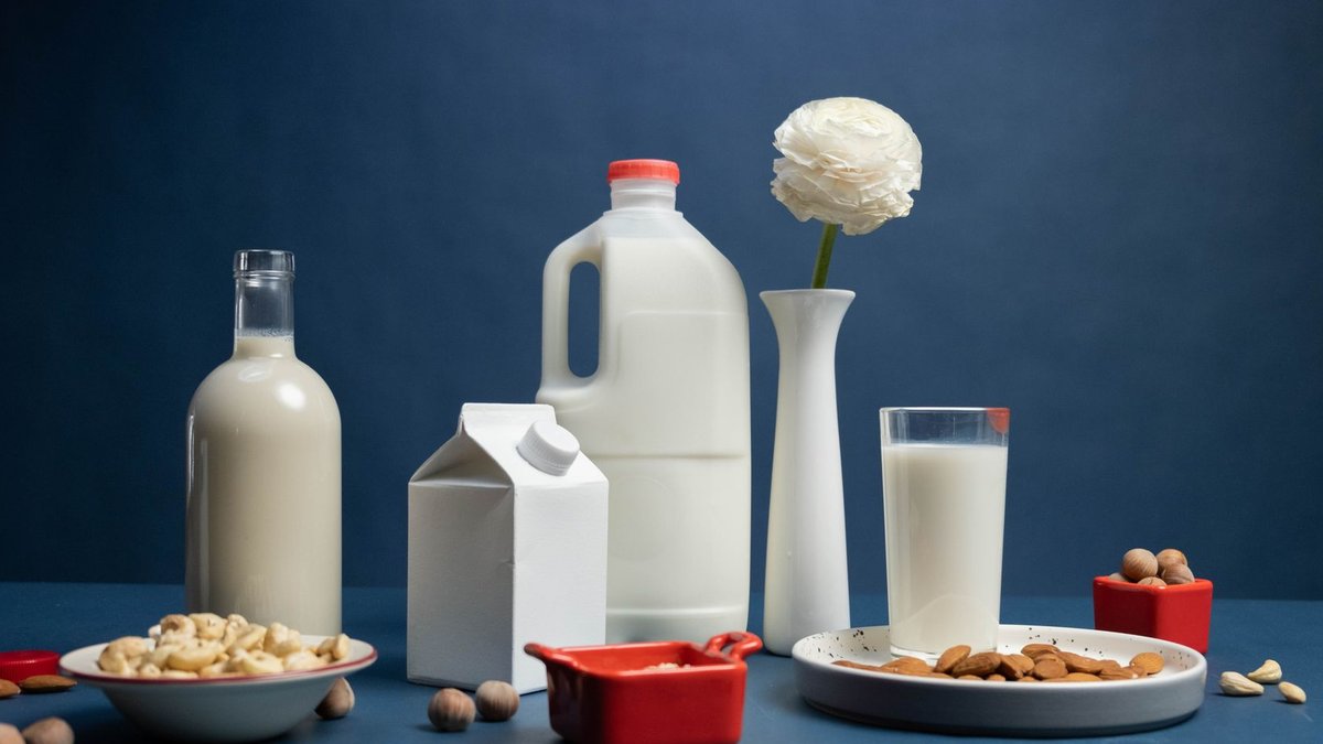 Still life of assorted vegan nut milks with nuts and decorative flower in studio.