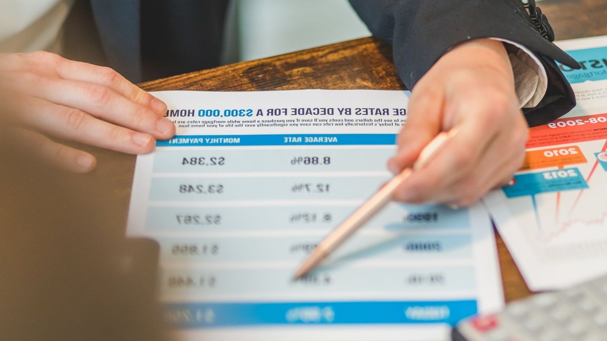 Central Banks Tighten Policy as Energy Costs Rise A close-up of hands analyzing mortgage rate documents with a pen and calculator in a business setting.