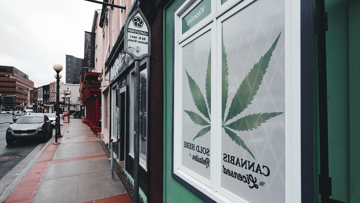 Street view of licensed cannabis retailer sign in urban setting with storefronts and cars.