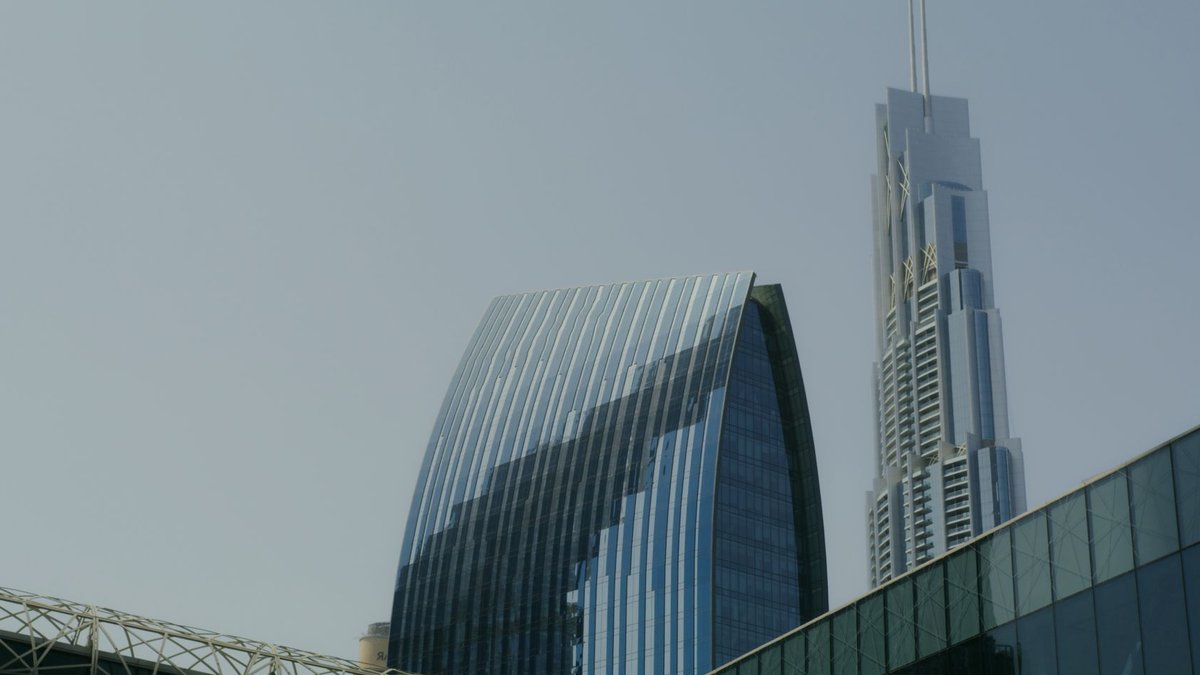 UAE Leads Global Construction with Dubai's Tower Boom Low-angle view of modern Dubai skyscrapers with glass facades against a clear sky.