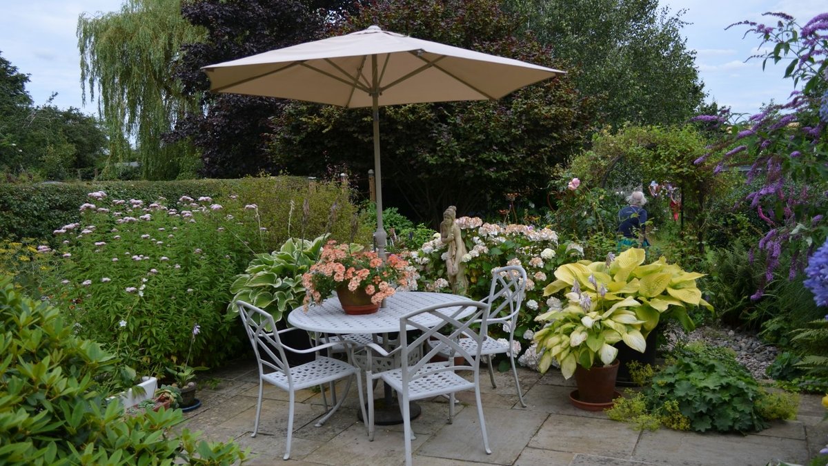 Chelsea Flower Show reveals People’s Choice winners A serene garden patio featuring a table with chairs, umbrella, and vibrant flowers in full bloom.