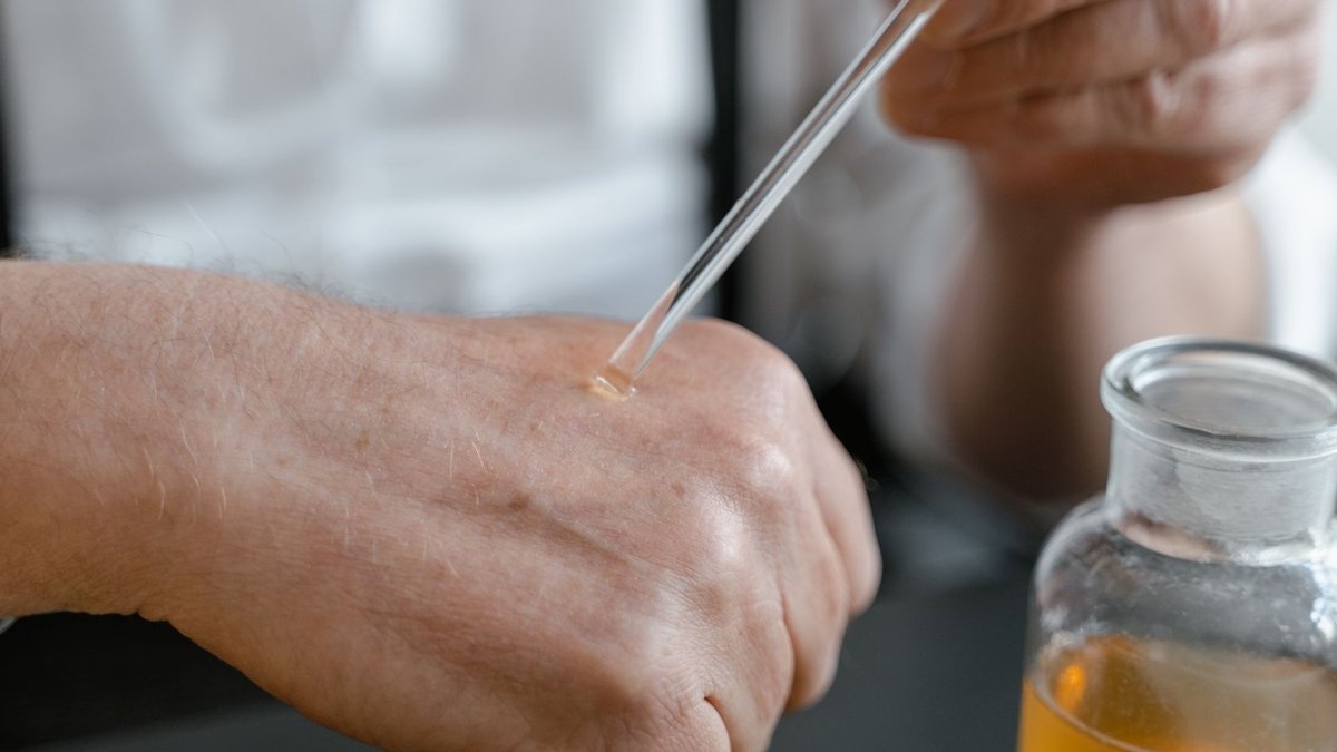 Dermatologists urged to reevaluate stubborn eczema diagnoses Close-up of a person applying perfume on their hand with a dropper, showcasing the art of fragrance testing.