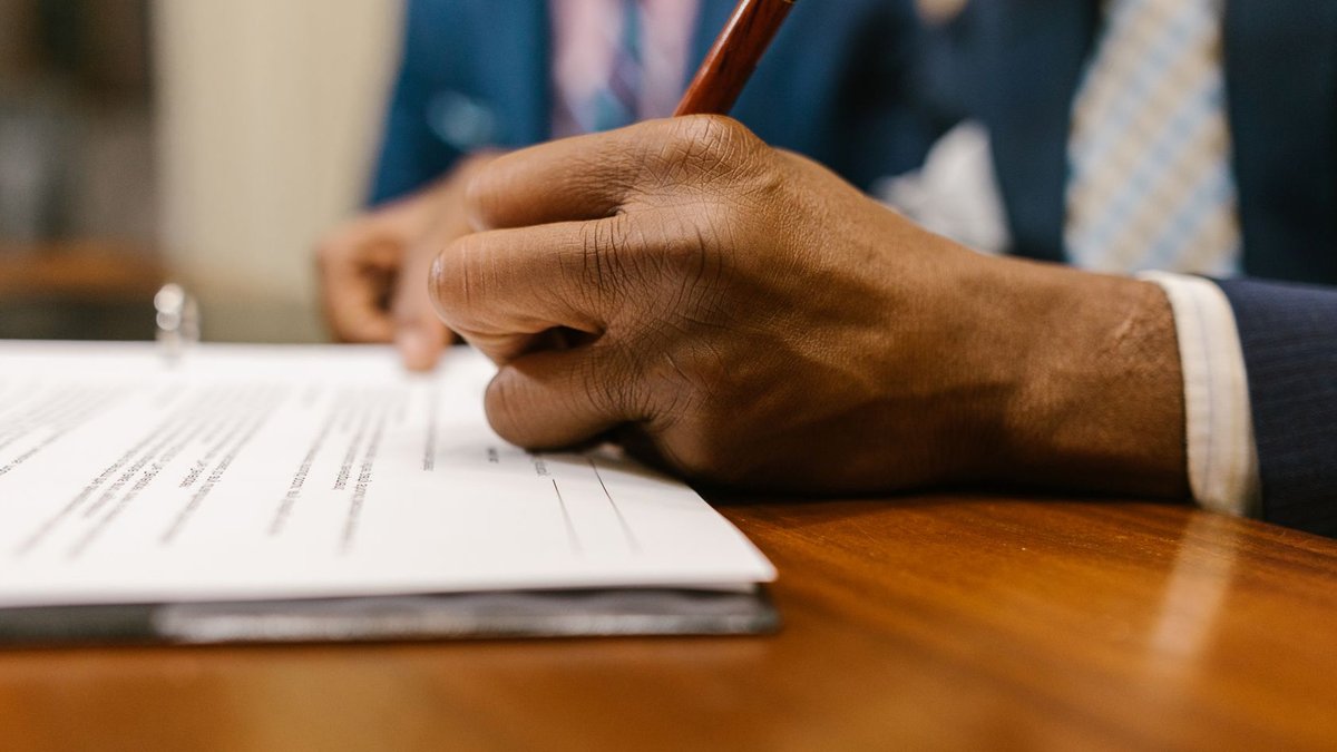 Close-up of an adult signing a legal document with a pen in an office.