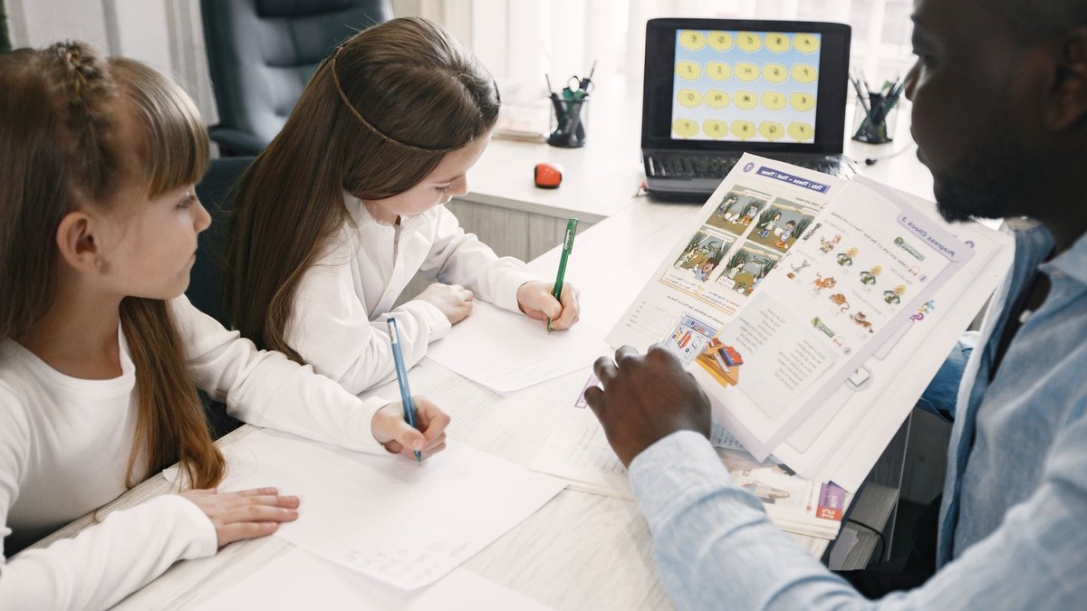 Weekly Guide Helps Teachers Manage School Year Stress A teacher instructing two young students in a classroom environment.