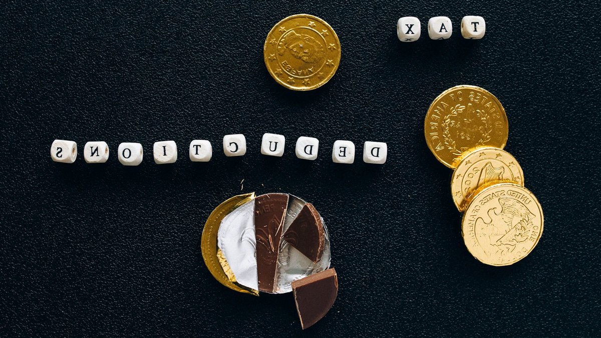 Creative concept of tax deductions using chocolate coins and letter tiles on a black background.