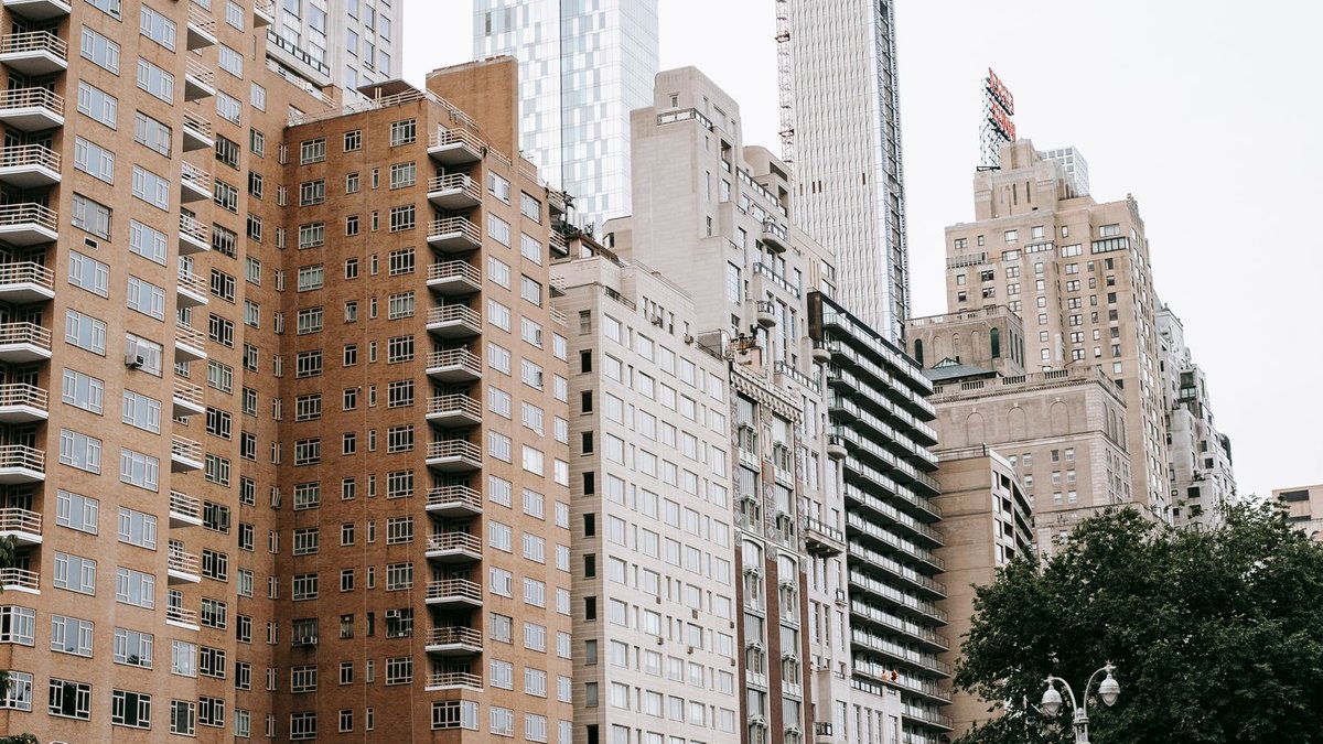 NYC Property Owners Battle Misapplied Pied-à-Terre Tax Facades of residential buildings located near modern skyscrapers on street in city with green trees against cloudless sky in