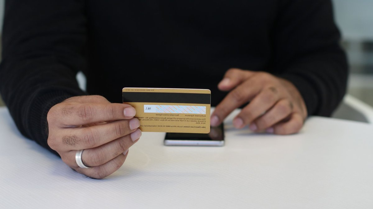 BlackRock's Preqin Deal Boosts Private Credit Transparency Person holding a credit card and smartphone, indoor close-up view.