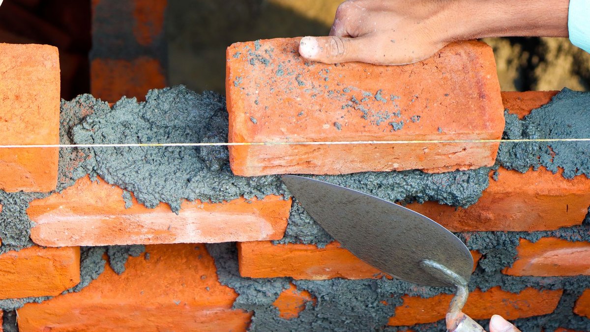 Hands laying bricks with cement in a construction setting, showcasing precise masonry work.