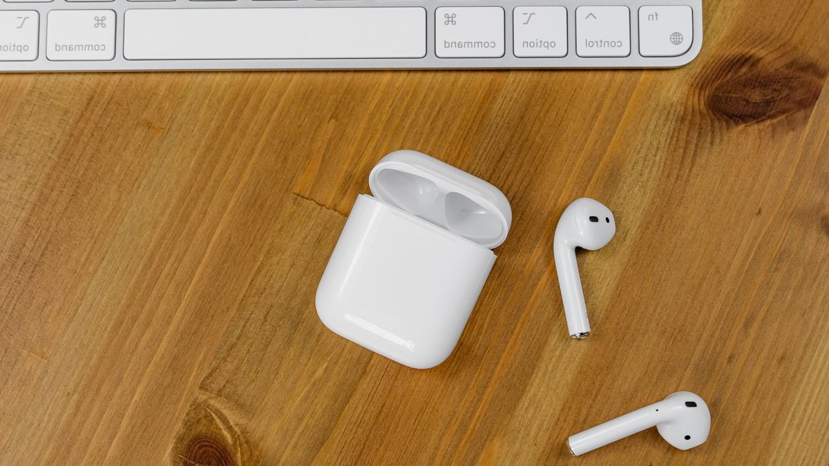 Apple Launches Smart Home Devices with LG Close-up view of wireless earbuds next to an Apple keyboard on a wooden desk surface.