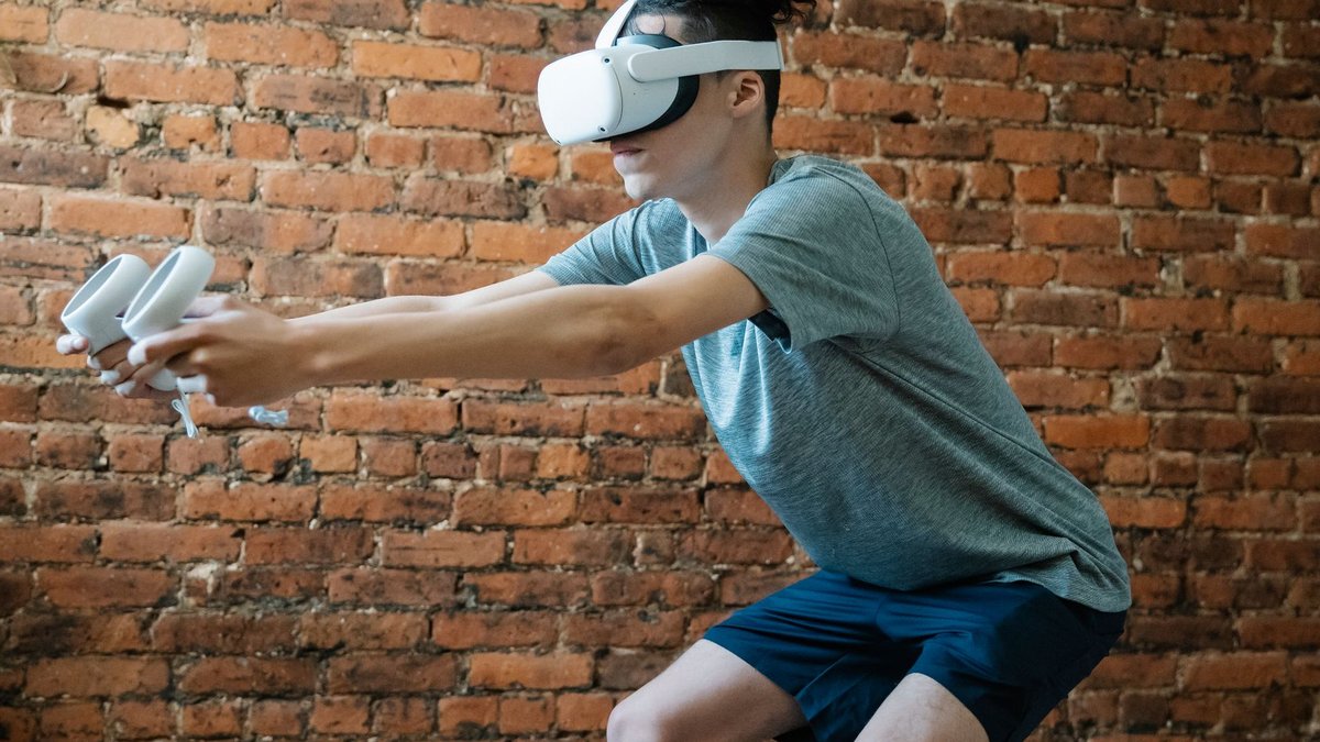 Side view of unrecognizable young male in casual clothes using goggles of virtual reality controlling with console while stan