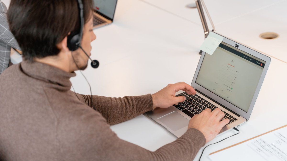 Call center agent wearing headphones working on a laptop in a modern office setting.