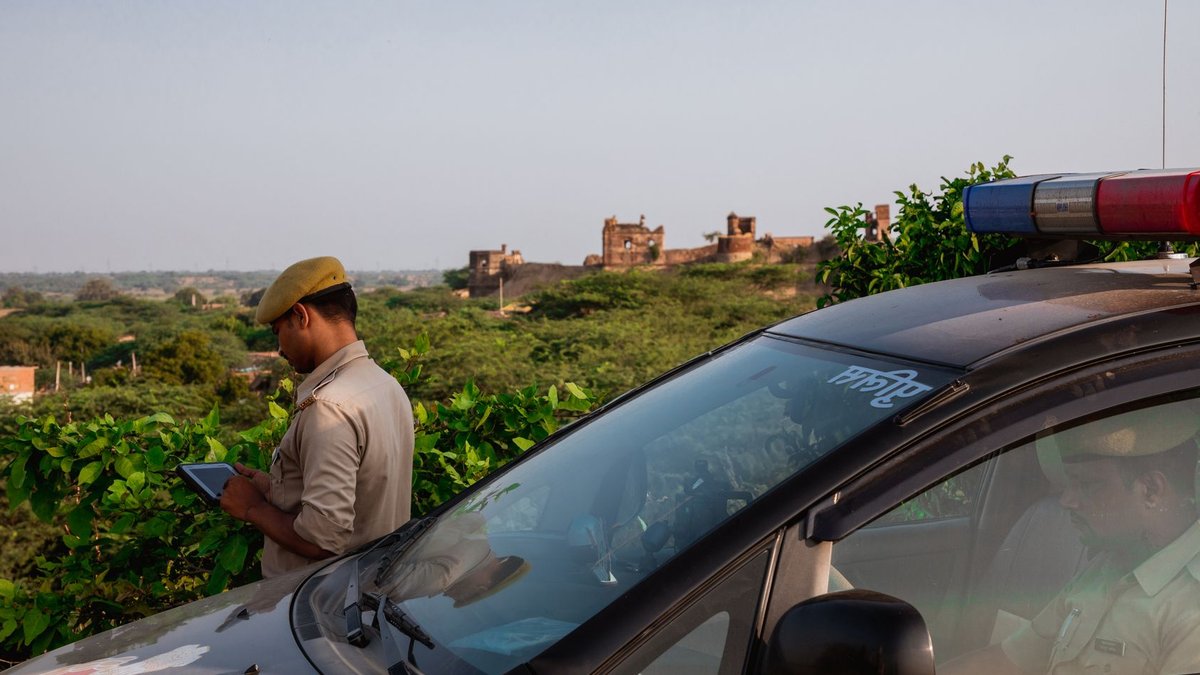 Police officer using tablet beside patrol car in scenic outdoor setting.