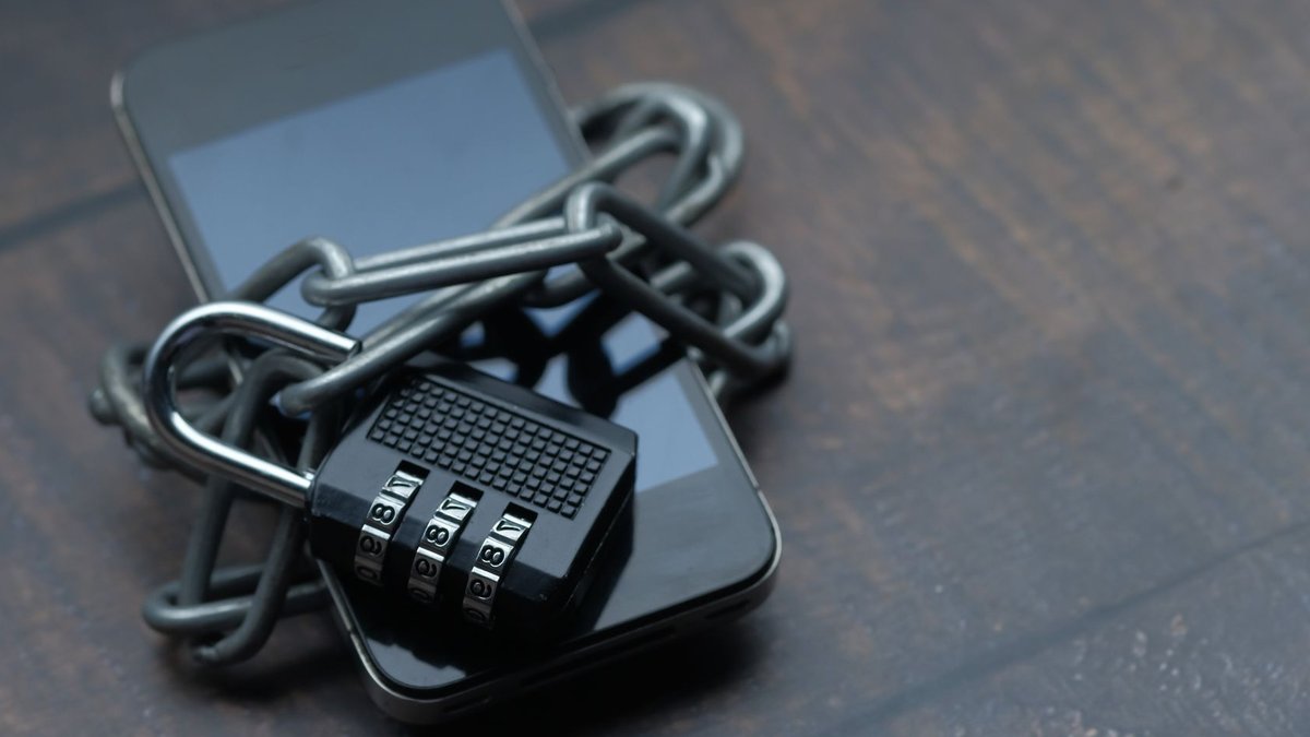 Close-up of a smartphone wrapped in a chain with a padlock, symbolizing strong security.