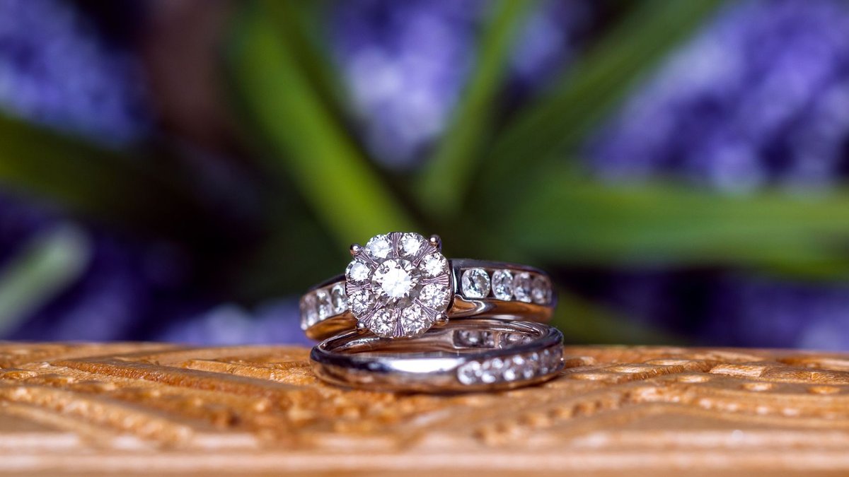Diamond Prices Edge Up, India's Jewelry Sales Surge 21% Close-up of diamond wedding rings on carved wood against a blurred floral background.