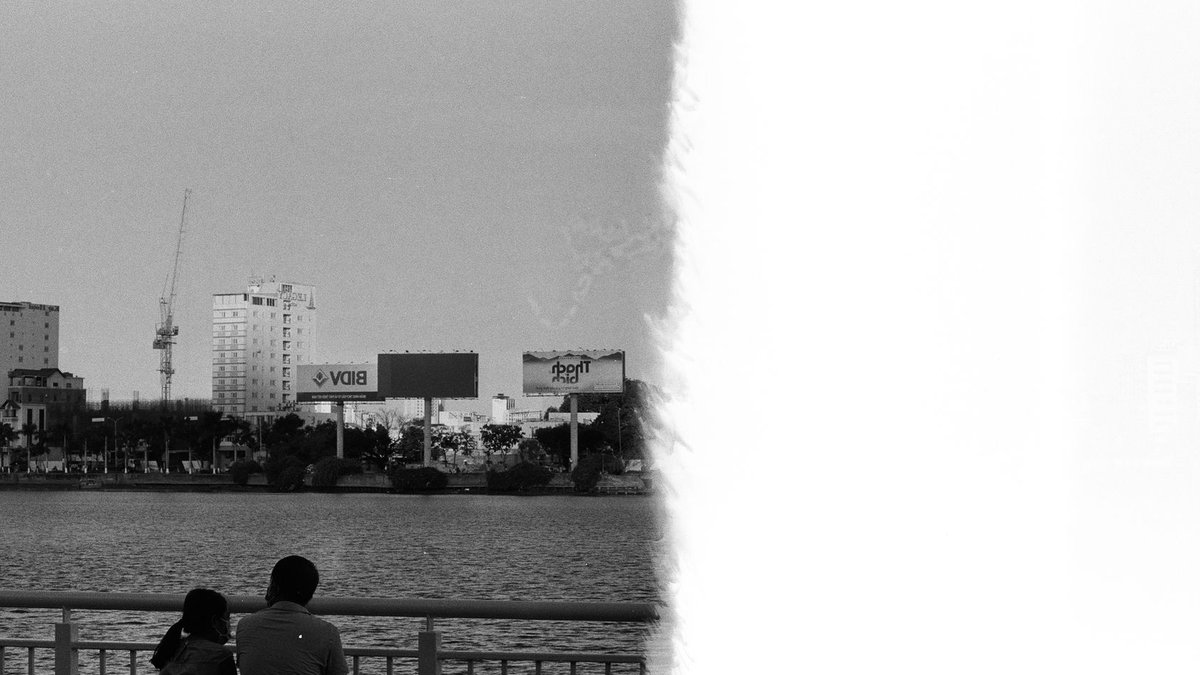 Monochrome image of a couple sitting by the Đà Nẵng river, viewing the city skyline.