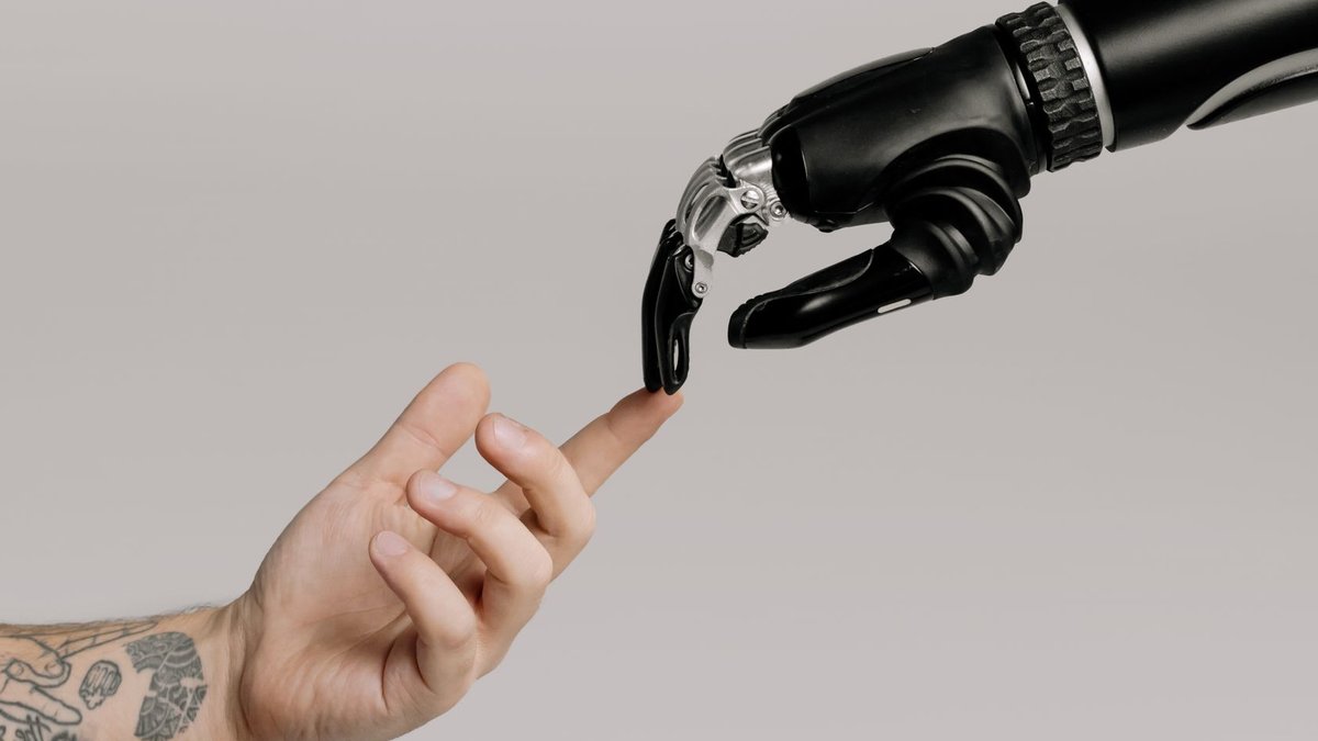 A human hand with tattoos reaching out to a robotic hand on a white background.