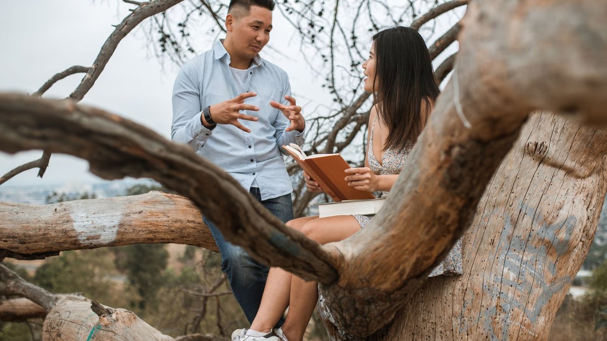 School leaders rethink authority for growth-driven conversations Asian couple enjoying a thoughtful conversation sitting on a tree branch outdoors.