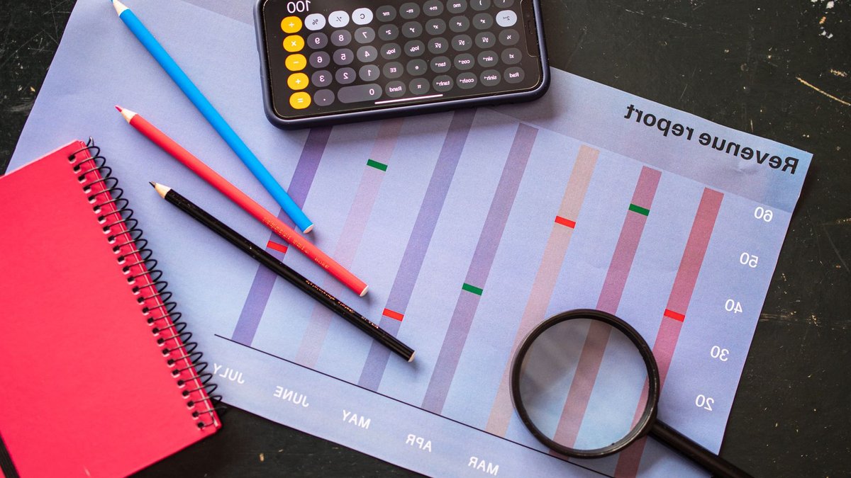 Flat lay of revenue report with a calculator, pencils, and notebook.