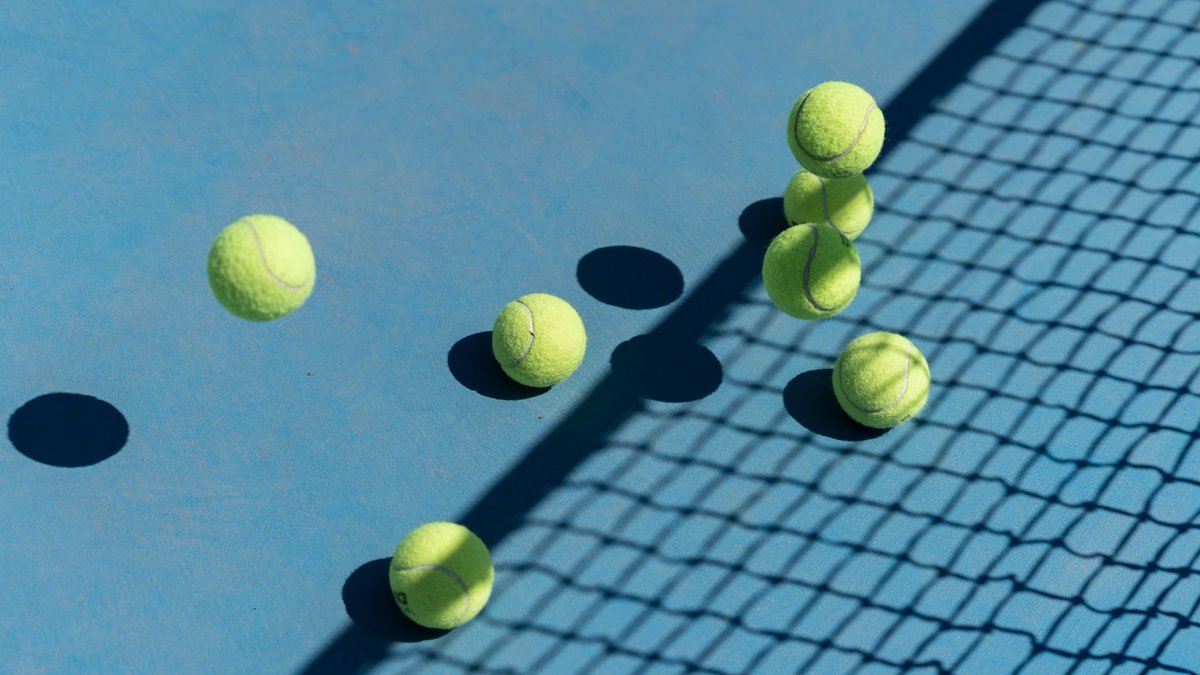 Australian Open to use AI for fan engagement and growth Tennis balls scattered on a blue court casting shadows, captured from above for a high-energy sports vibe.
