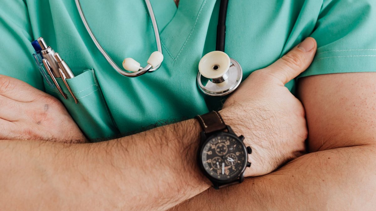 Unrecognizable female doctor in medical uniform with wristwatch on hand crossing arms on chest while standing with stethoscop