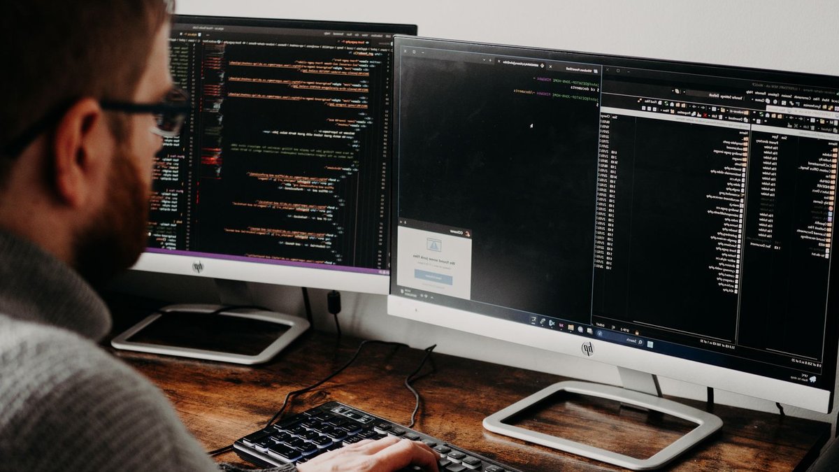 Early code scans cut breach risks far cheaper Software developer typing code on dual monitors at a wooden desk.